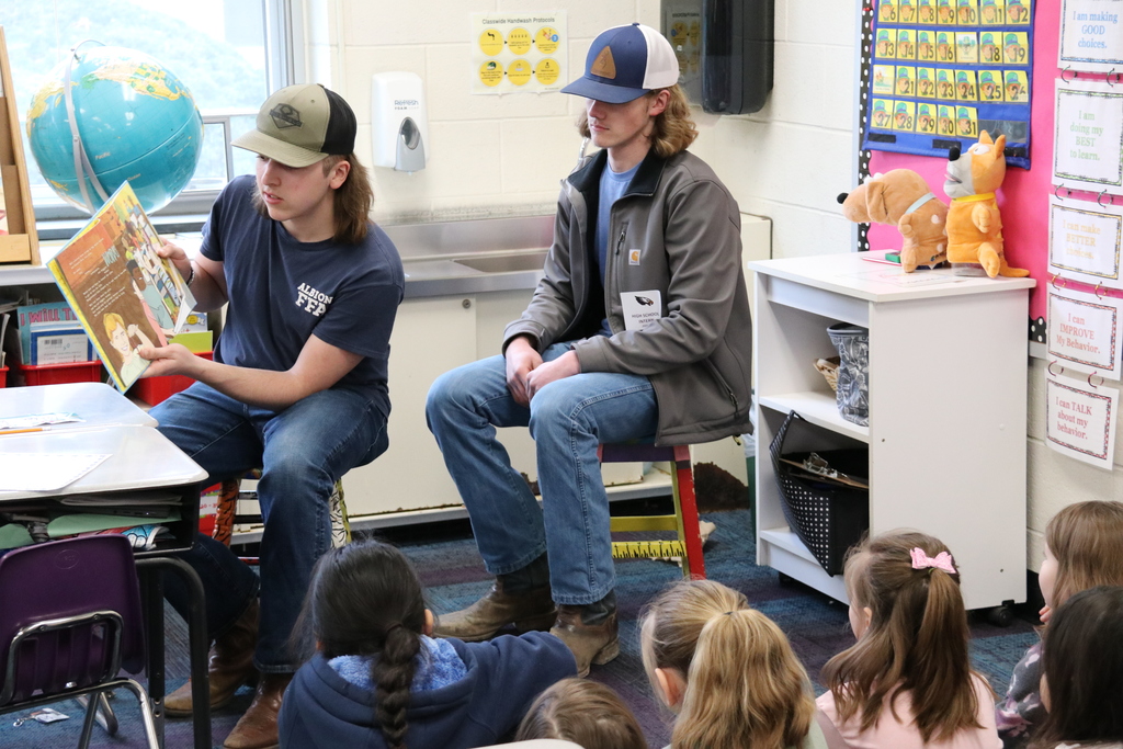 two high school students read a book to an elementary class