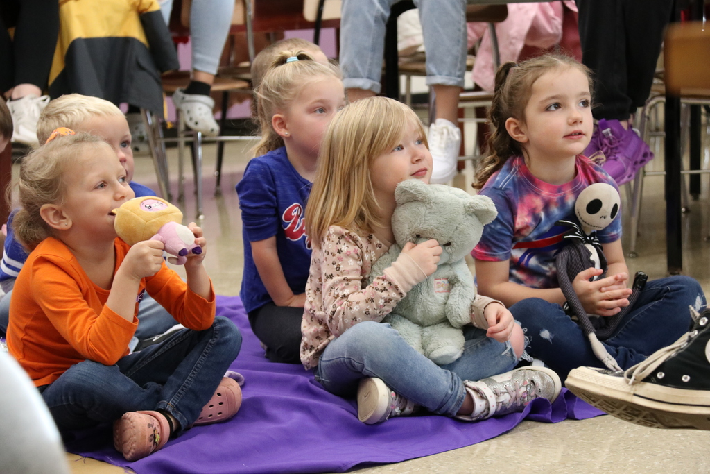 students listen to a story while holding stuffed animals